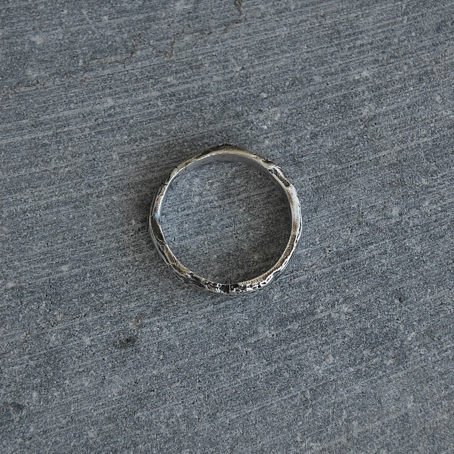 Bijou brut en argent, au design organique et irrégulier, capturé sur fond naturel.