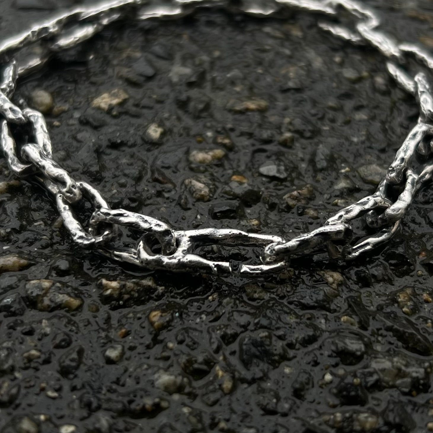 Gros plan sur les maillons irréguliers d’un bracelet chaîne artisanal en argent massif texturé